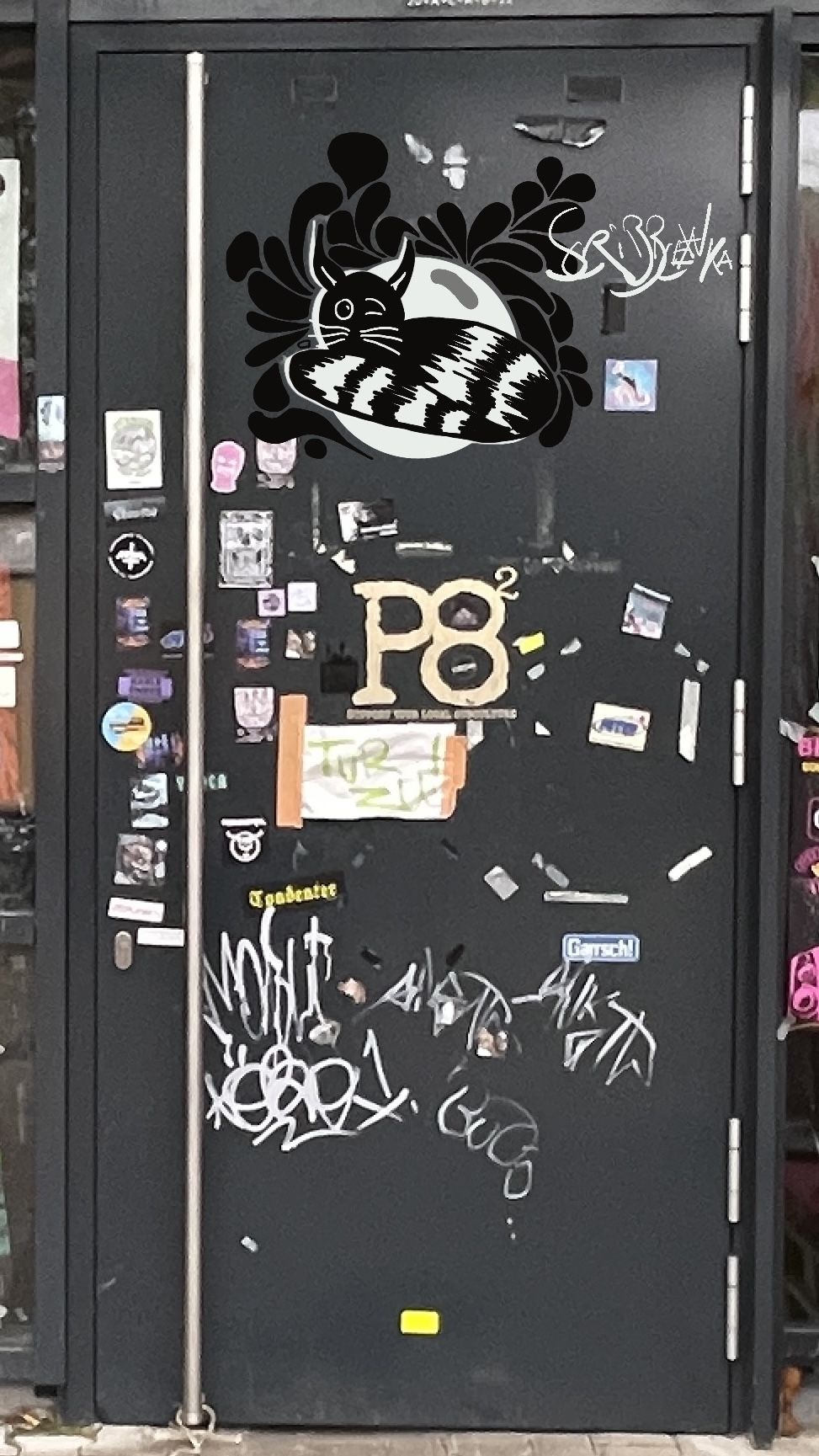 Die Tür des Kulturzentrums P8 in der Schauenburgstraße. Es zeigt verschiedene Graffitis. Unter anderem eine zwinkernde schwarzweiße Katze.