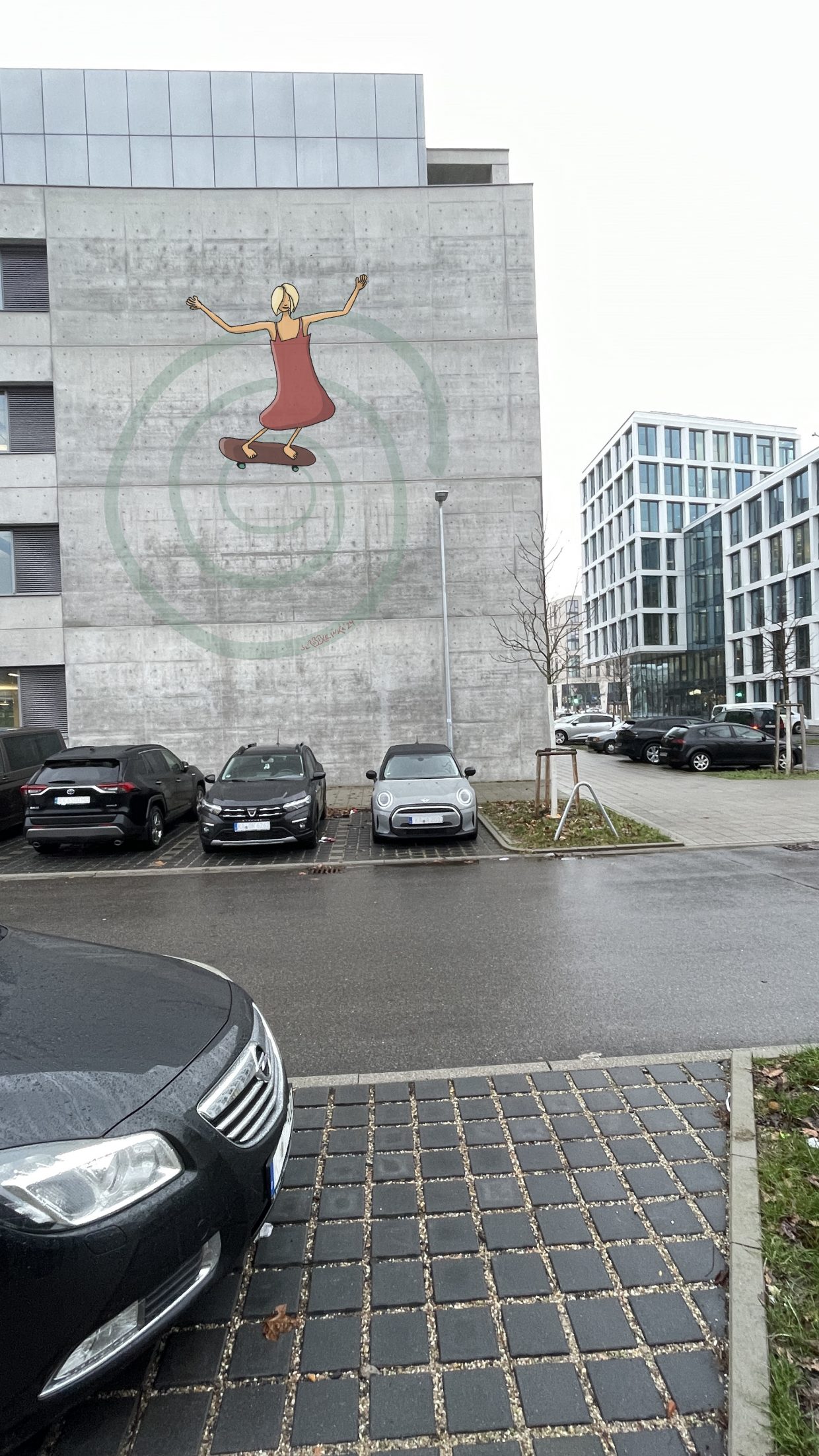 Parkplatz in Karlsruhe vor einem Bürogebäude. Auf der Außenwand ist ein Gemälde, das eine Skaterin zeigt.