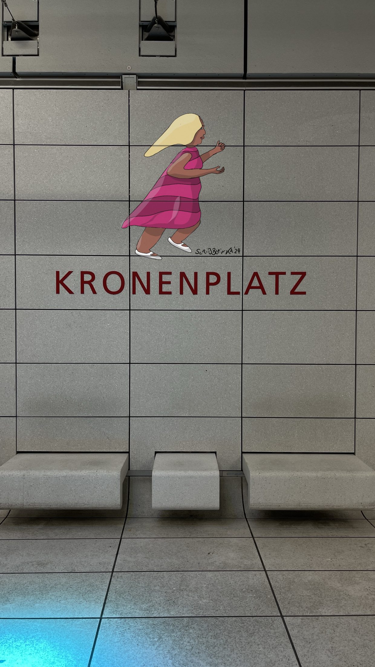 Haltestelle Kronenplatz in Karlsruhe. Man sieht über der Aufschrift Kronenplatz an der Wand das Gemälde einer eilenden Frau in einem pinkfarbenen, gestreiften Kleid.